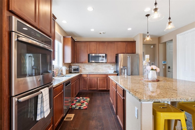 kitchen featuring stainless steel appliances, brown cabinets, dark wood-style flooring, light stone counters, and a sink