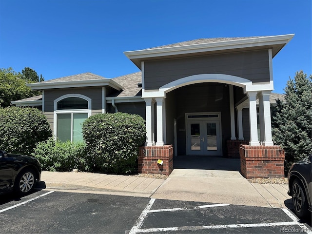 doorway to property with french doors, uncovered parking, and roof with shingles