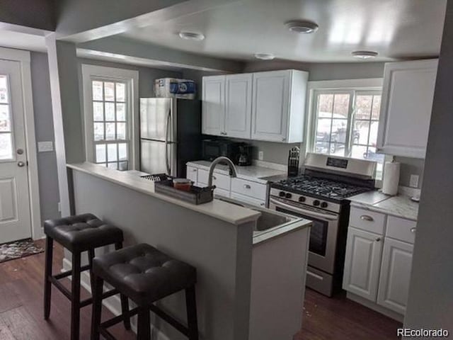 5725 W Mississippi Ave, Lakewood, CO 80226 - kitchen with appliances with stainless steel finishes, a kitchen breakfast bar, dark wood-style flooring, white cabinetry, and healthy amount of natural light