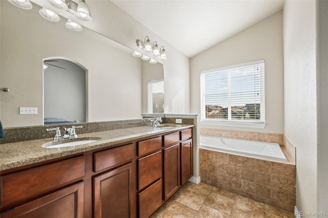 bathroom featuring ceiling fan, a relaxing tiled tub, vanity, and lofted ceiling