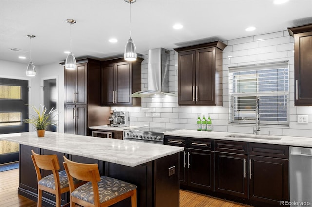 kitchen featuring wall chimney range hood, appliances with stainless steel finishes, a breakfast bar, light wood-style floors, and recessed lighting