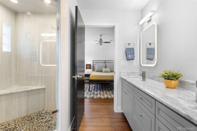 ensuite bathroom featuring tiled shower, wood finished floors, double vanity, and a ceiling fan