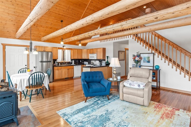 living room featuring light wood-type flooring, a wood stove, sink, beamed ceiling, and wooden ceiling