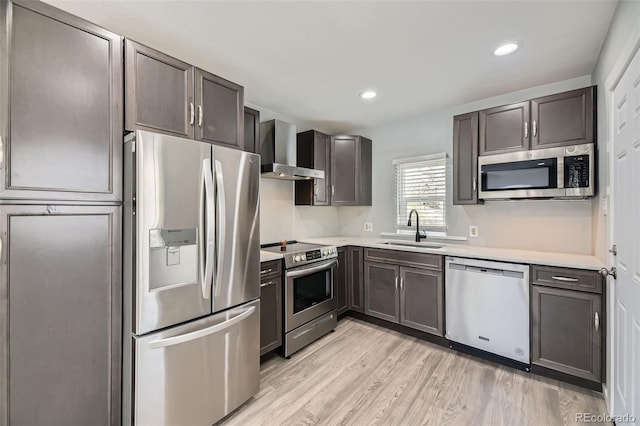kitchen with stainless steel appliances, wall chimney exhaust hood, a sink, light countertops, and light wood finished floors