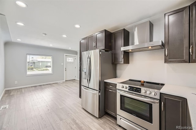 kitchen featuring appliances with stainless steel finishes, wall chimney exhaust hood, light countertops, light wood finished floors, and dark brown cabinets
