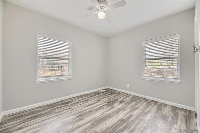 spare room with wood finished floors, a ceiling fan, and baseboards