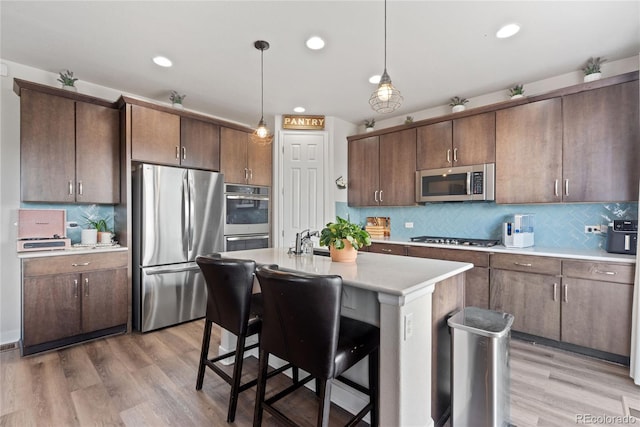 kitchen with appliances with stainless steel finishes, light countertops, tasteful backsplash, light wood finished floors, and a kitchen breakfast bar