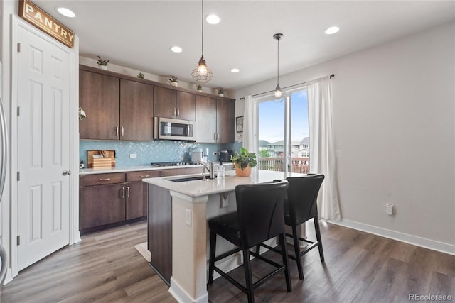kitchen with stainless steel microwave, light countertops, decorative backsplash, wood finished floors, and recessed lighting