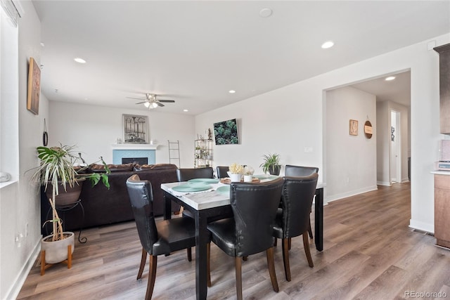 dining space featuring a ceiling fan, light wood-style floors, a fireplace, baseboards, and recessed lighting