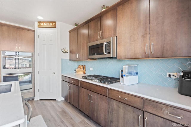 kitchen with stainless steel appliances, light countertops, light wood-style flooring, and tasteful backsplash
