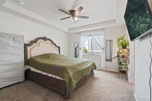 carpeted bedroom featuring a raised ceiling, a ceiling fan, and baseboards