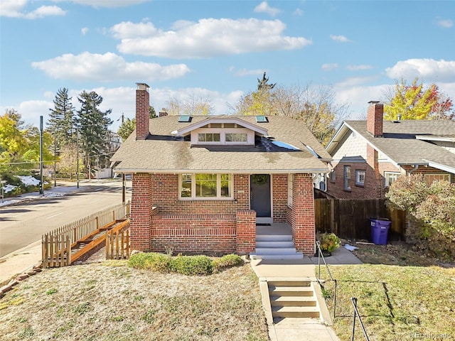 bungalow-style home featuring a shingled roof, a chimney, stairway, fence, and brick siding