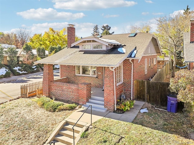 bungalow featuring a shingled roof, a chimney, fence, and brick siding