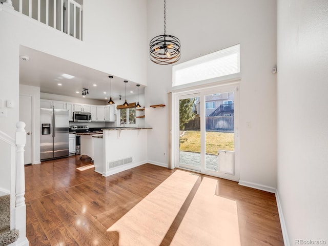 kitchen with dark wood-type flooring, kitchen peninsula, pendant lighting, stainless steel appliances, and white cabinets