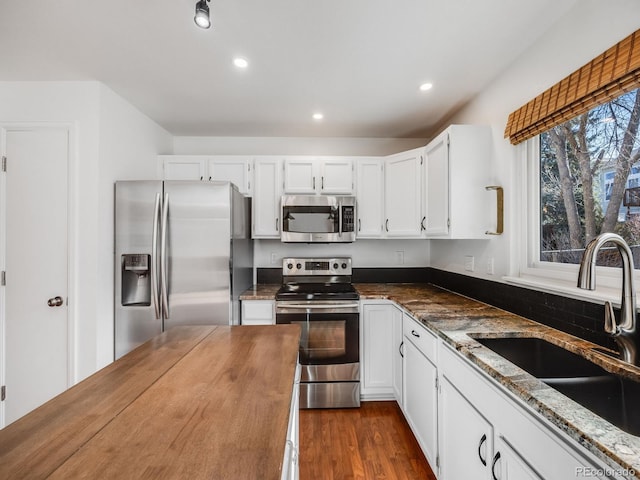 kitchen with white cabinetry, appliances with stainless steel finishes, sink, and dark stone counters