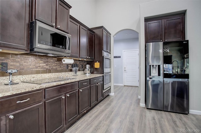 25525 E 1st Ave, Aurora, CO 80018 - kitchen with appliances with stainless steel finishes, light wood-style floors, backsplash, dark brown cabinets, and arched walkways