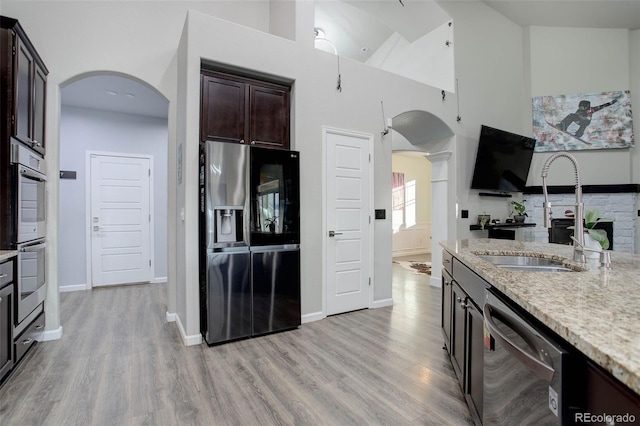 25525 E 1st Ave, Aurora, CO 80018 - kitchen with stainless steel appliances, arched walkways, dark brown cabinets, light stone counters, and light wood-style flooring