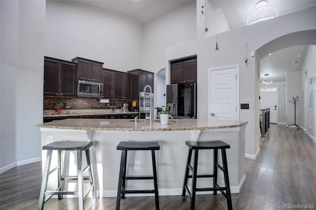 25525 E 1st Ave, Aurora, CO 80018 - kitchen with stainless steel microwave, arched walkways, dark brown cabinets, a center island with sink, and a towering ceiling