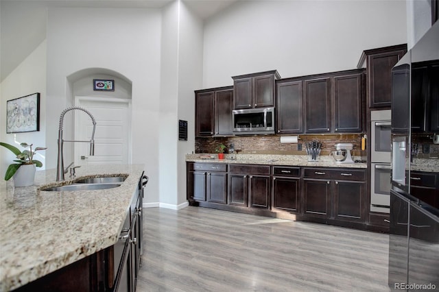 25525 E 1st Ave, Aurora, CO 80018 - kitchen with appliances with stainless steel finishes, backsplash, light stone countertops, a towering ceiling, and light wood-style flooring