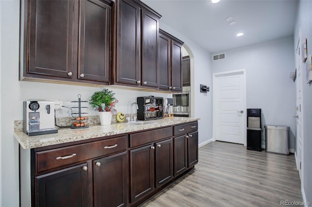 25525 E 1st Ave, Aurora, CO 80018 - kitchen featuring dark brown cabinets, arched walkways, light wood finished floors, recessed lighting, and light stone counters