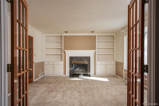 unfurnished living room with a fireplace, built in features, and light carpet