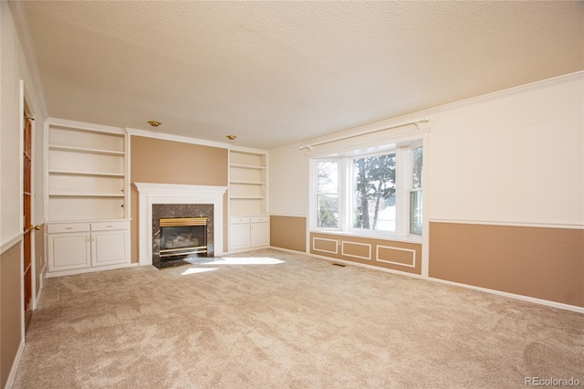 unfurnished living room with a high end fireplace, carpet floors, ornamental molding, and a textured ceiling