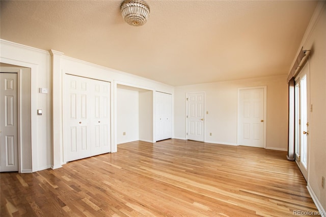 unfurnished bedroom with multiple closets, ornamental molding, and light hardwood / wood-style flooring