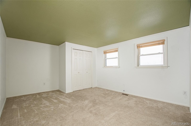 unfurnished bedroom with a closet, a textured ceiling, and light colored carpet