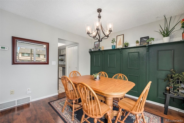 dining space with a textured ceiling, visible vents, wood finished floors, baseboards, and a chandelier