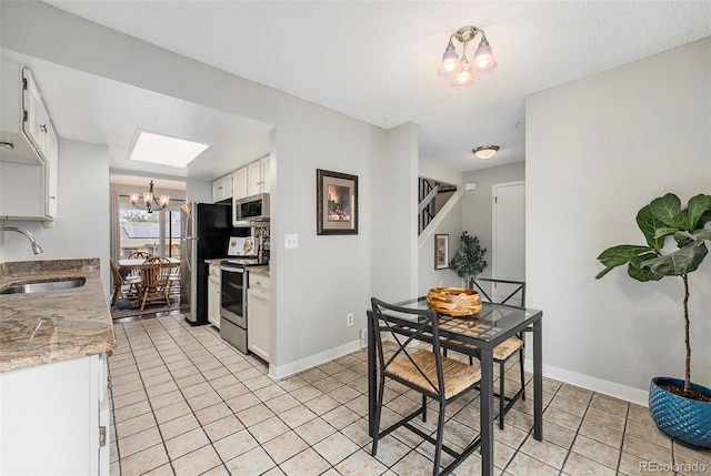 kitchen with light tile patterned flooring, white cabinetry, a sink, appliances with stainless steel finishes, and a notable chandelier