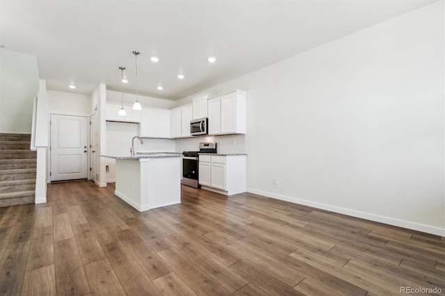 kitchen with white cabinetry, light stone counters, an island with sink, appliances with stainless steel finishes, and hardwood / wood-style flooring