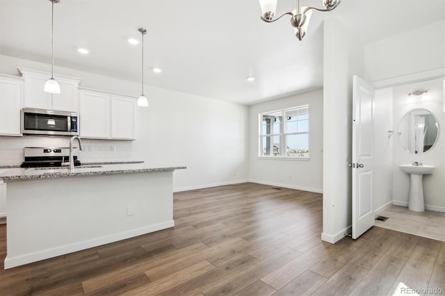 kitchen featuring light stone countertops, hanging light fixtures, stainless steel appliances, hardwood / wood-style floors, and white cabinets