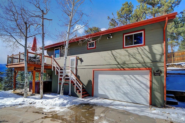 snow covered back of property featuring a garage and a deck