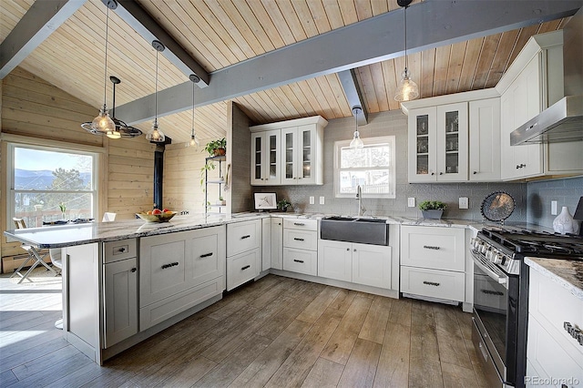 kitchen featuring decorative light fixtures, white cabinetry, sink, stainless steel range with gas stovetop, and wall chimney range hood