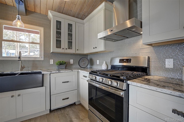 kitchen featuring stainless steel gas stove, white cabinetry, decorative light fixtures, ventilation hood, and light stone countertops