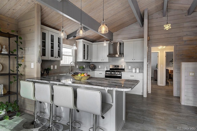 kitchen featuring stainless steel range with gas cooktop, pendant lighting, white cabinetry, light stone counters, and wall chimney exhaust hood