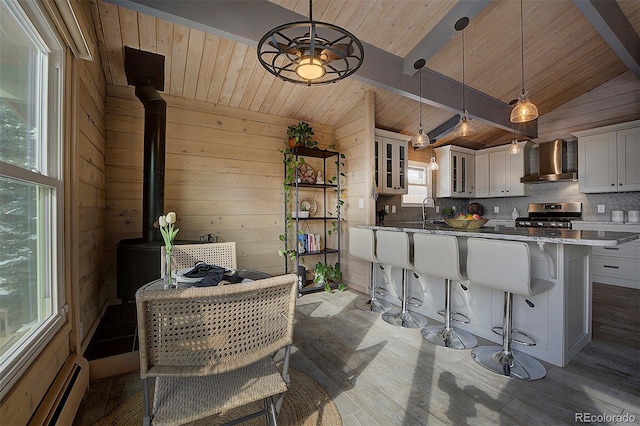 kitchen with lofted ceiling with beams, stainless steel stove, white cabinets, pendant lighting, and wall chimney range hood