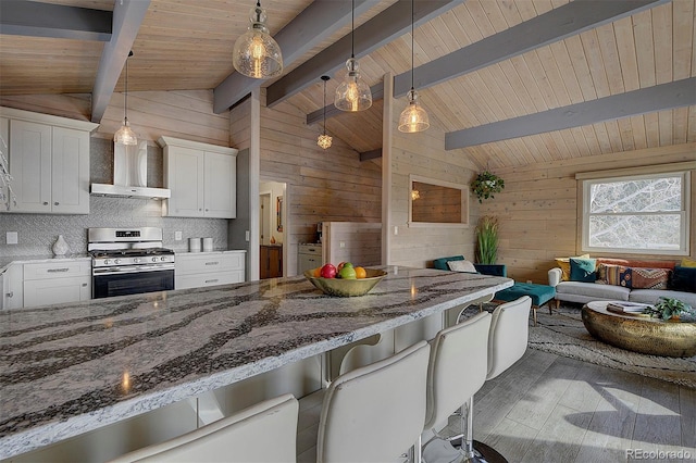 kitchen with white cabinets, a kitchen bar, stainless steel gas range oven, wall chimney range hood, and wooden ceiling