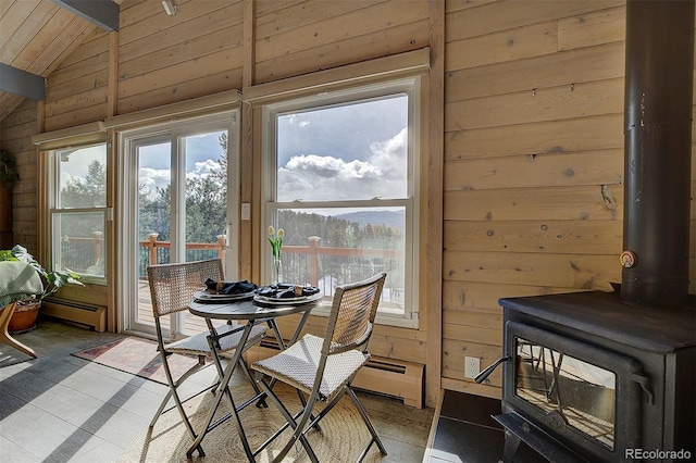 dining room featuring a baseboard heating unit, lofted ceiling, a wood stove, and wooden walls