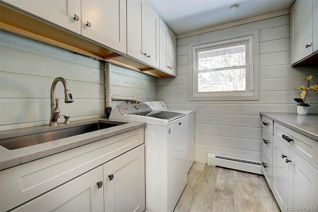 clothes washing area with sink, cabinets, light hardwood / wood-style flooring, a baseboard radiator, and washer and clothes dryer