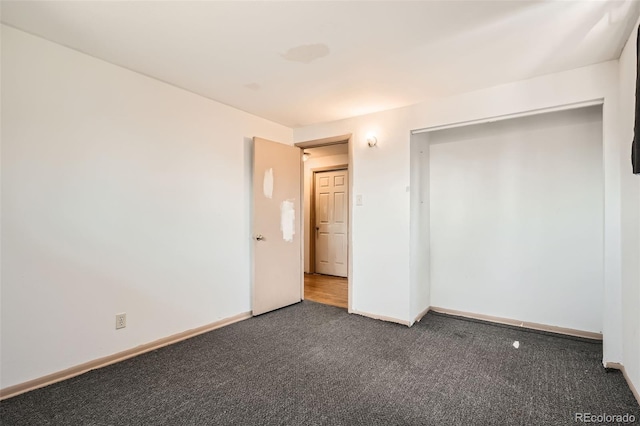 unfurnished bedroom with dark carpet and baseboards