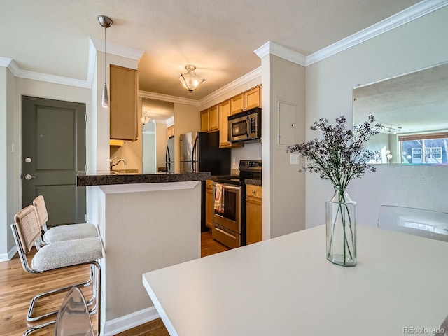 kitchen with appliances with stainless steel finishes, crown molding, pendant lighting, and hardwood / wood-style floors