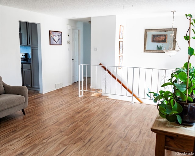 sitting room with visible vents, a textured ceiling, wood finished floors, and an upstairs landing