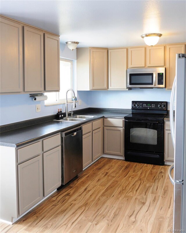 kitchen featuring stainless steel appliances, dark countertops, a sink, and light wood-style floors