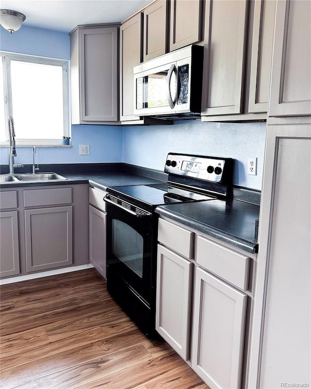 kitchen featuring dark countertops, a sink, gray cabinetry, stainless steel microwave, and black range with electric cooktop