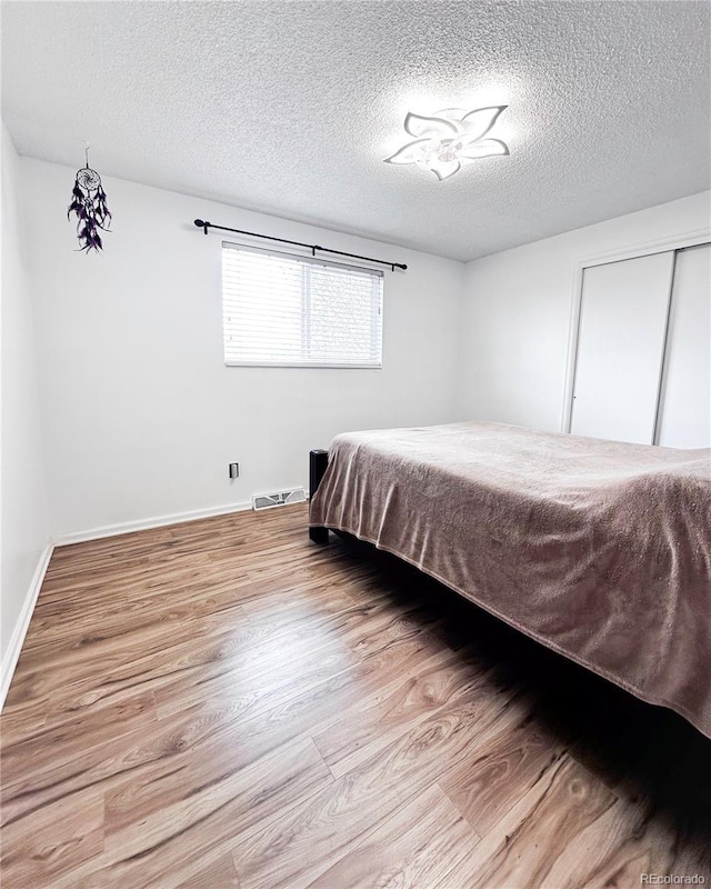 bedroom featuring baseboards, a textured ceiling, visible vents, and wood finished floors