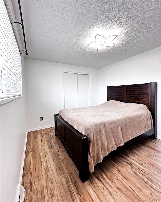 bedroom with light wood-style floors, baseboards, a closet, and a textured ceiling