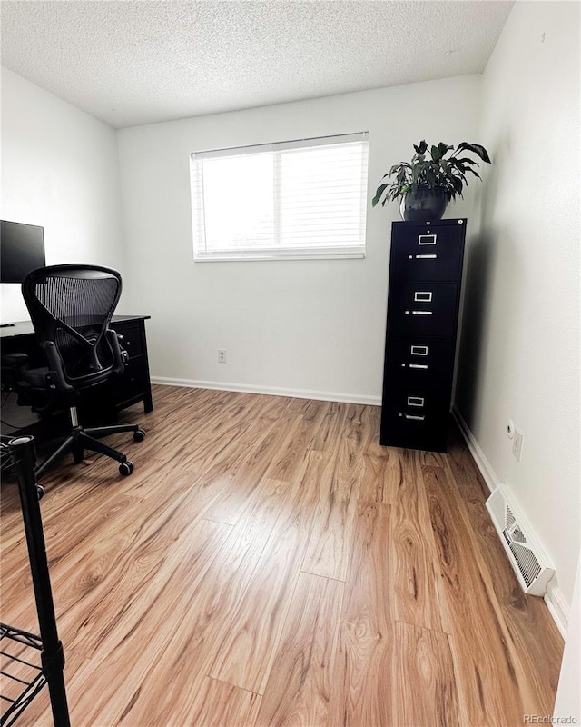 office space with a textured ceiling, baseboards, light wood-style flooring, and visible vents