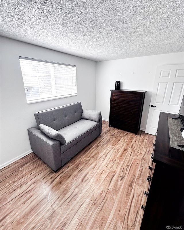 living area with baseboards, light wood-type flooring, and a textured ceiling