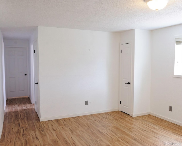 unfurnished room with a textured ceiling, baseboards, and light wood-style floors